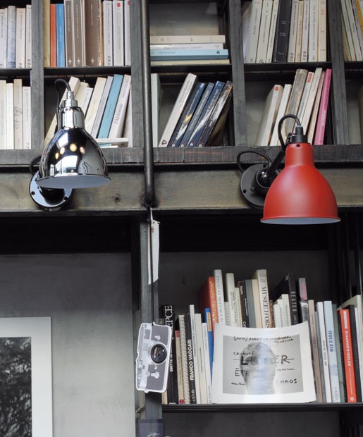Wandspot La Lampe Gras op de boekenkast, links een verchroomde kap en rechts een gematteerde rode kap